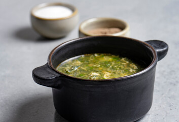 Soup with green sorrel in black ceramic pot on gray background