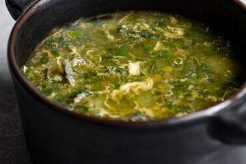 Soup with green sorrel in black ceramic pot on gray background