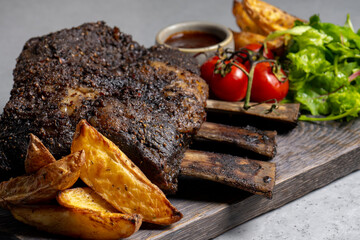 grilled pork ribs with french fries and vegetables on a wooden board