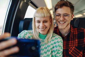 A cheerful travelers sitting in a train and taking selfies.