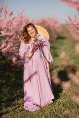 Woman blooming peach orchard. Against the backdrop of a picturesque peach orchard, a woman in a long pink dress and hat enjoys a peaceful walk in the park, surrounded by the beauty of nature.