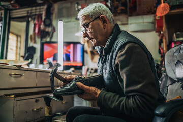 Side view of a senior craftsman repairing footwear at workshop.