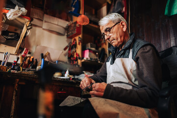 An old artisan cutting with scissors at his workshop.