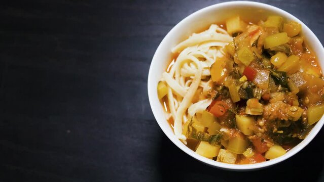Stewed vegetables with meat and noodles in a bowl. Lagman. Black background.