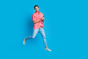 Fototapeta na wymiar Full size photo of intelligent man dressed striped shirt denim pants run empty space hold smartphone isolated on blue color background