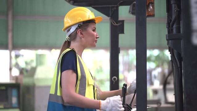 caucasian Industry engineer worker woman wearing safety uniform and hard hat control stick of truck crane or forklift In Industrial Factory warehouse .