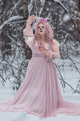 Obraz na płótnie Canvas A beautiful spring fairy, a dryad with deer antlers and a crown and a light pink dress in a snowy forest.A fabulous photo. The concept of changing seasons.