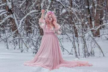 A beautiful spring fairy, a dryad with deer antlers and a crown and a light pink dress in a snowy forest.A fabulous photo. The concept of changing seasons.