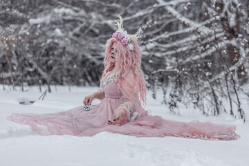 A beautiful spring fairy, a dryad with deer antlers and a crown and a light pink dress in a snowy...