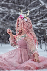 A beautiful spring fairy, a dryad with deer antlers and a crown and a light pink dress in a snowy...