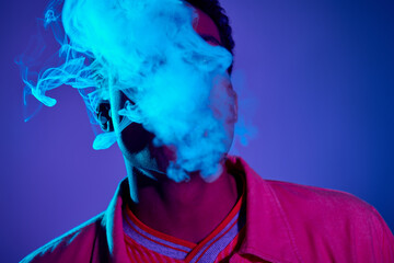 handsome african american man exhaling smoke against blue background with purple lighting, gen z © LIGHTFIELD STUDIOS