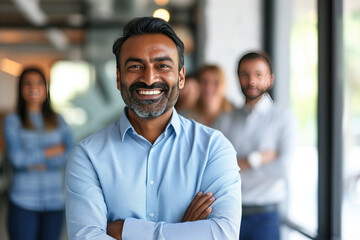 Smiling Indian businessman executive with a team in the background at a modern corporate office