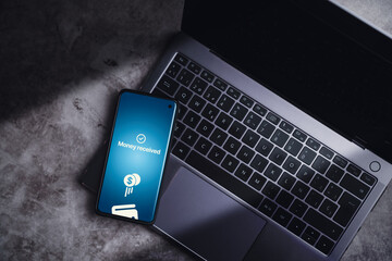 Smartphone resting on laptop with money transferred online on screen. Concept of financial transactions with mobile devices. Smartphone screen displaying money transfer confirmation.