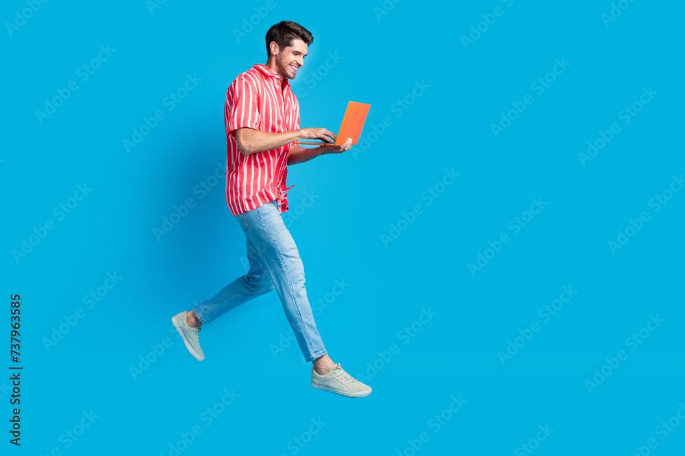 Poster full size photo of smart man dressed striped shirt denim pants hurry run empty space texting on lapt