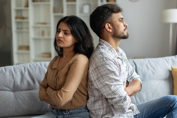 Indian couple sitting back to back on couch at home, upset spouses offended after quarrel, suffering problems in relationship
