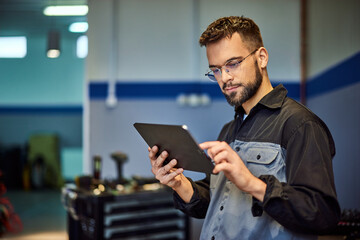 A concentrated auto mechanic, using a digital tablet at his workplace.