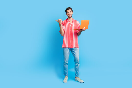 Full body photo of clever guy wear stylish shirt jeans hold laptop indicating at promo empty space isolated on blue color background