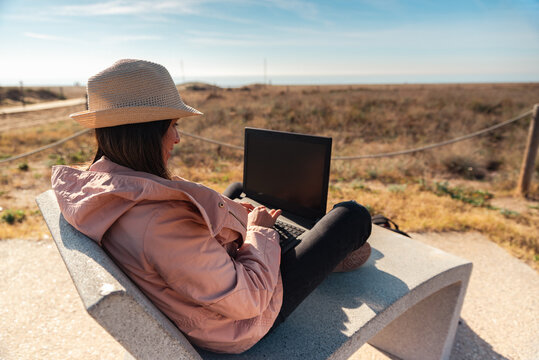 Traveler with her laptop sitting on the Mediterranean coast of Barcelona.