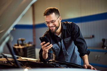 A smiling mechanic receives a message on his phone while working at his car service.