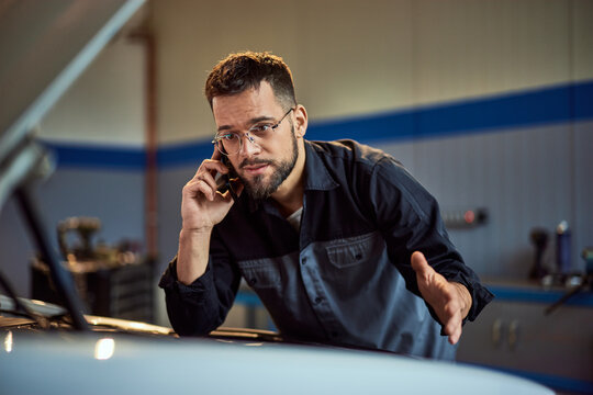 A mechanic man is making a phone call while having a car problem at his repair car service.