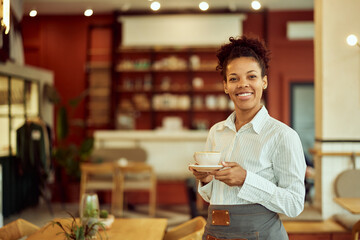 Portrait of a smiling African waitress, holding a cup of coffee.