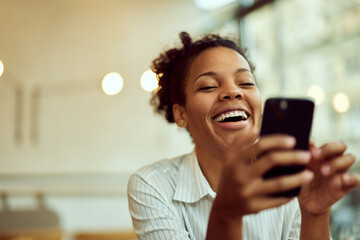 Curly-haired African female, using a mobile phone, watching something online, and laughing.