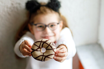 Happy little school girl eating sweet donut at homey. Blond child with doughnut. Cute kid with...