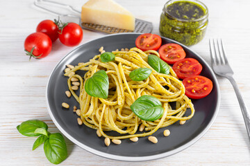Pasta pesto, spaghetti with pesto sauce and fresh basil leaves in black plate on white wooden background served with food ingredients. Traditional italian cuisine.