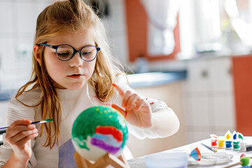 Little girl painting globe or ball with colors. School child making earth globe for school project....