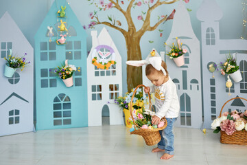 Baby girl celebrate Easter. Funny happy kid in bunny ears playing on Easter egg hunt. Family home decoration, colorful Easter eggs and flowers. Home decoration and flowers - obrazy, fototapety, plakaty