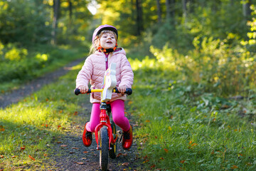 Child riding balance bike. Kids on bicycle in sunny forest. Little girl enjoying to ride glider bike on warm day. Preschooler learning to balance on run bicycle in safe helmet. Sport activity