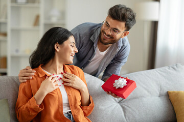 Loving hindu husband giving present gift box to his beloved wife, celebrating birthday, having...