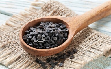 The Poppy seeds in a wooden spoon on a white table and burlap