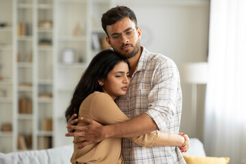 Loving indian man hugging, comforting and supporting his wife feeling sad and depressed, unhappy couple having relationship trouble
