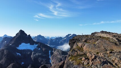 Tiny human standing on edge of cliff in the mountains