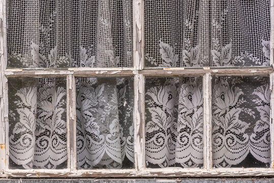 Detail eines verwitterten Holzkastenfensters mit Gardinen