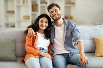 Loving indian spouses embracing, sitting on sofa in modern living room, husband hugging his wife...