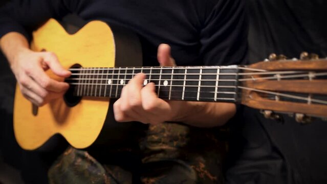 Playing an acoustic guitar on a black background. The musician clamps the frets of the guitar on the neck. Musical instrument in male hands. Close-up. Soft focus.