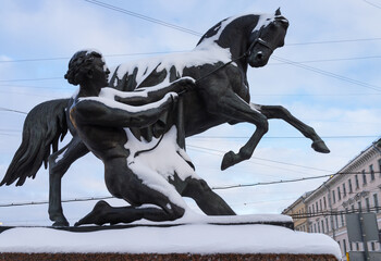 Saint Petersburg on snowy winter day. View of the famous Anichkov Bridge with beautiful sculptures by Peter Klodt Taming Horses across  Fontanka River on Nevsky Prospekt on sunny cold day