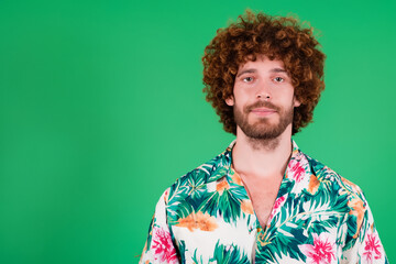 Fototapeta na wymiar male model. portrait of a curly-haired man in a colored shirt, green background. hawaii and fashion concept