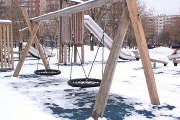 Wooden playground made of natural eco-friendly material in public city park with snow at winter time. Modern safety children outdoor equipment. Winter activities. Children rest and games on open air