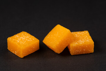 Heap of mango candy cubes on dark background.