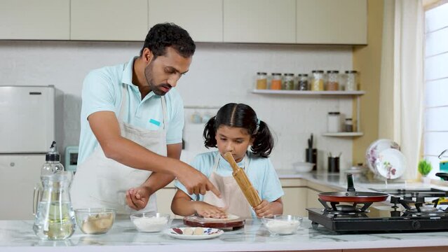 Joyful Indian father with Kid preparing Chapati by preparing flour at kitchen - concept of family cooking, parental caring and loving relationship.