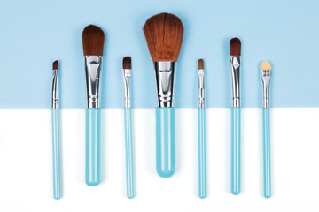 Set of makeup brushes on blue and white colored composed background. Top view point, flat lay.