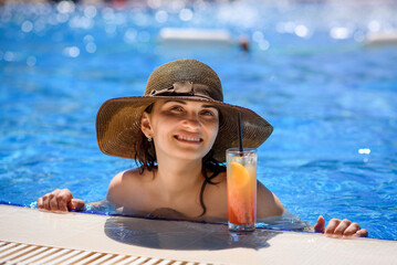 woman with a hat in the swimming pool drinking a cocktail..