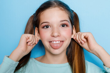 little girl grimacing and having fun at camera isolated over blue background. - obrazy, fototapety, plakaty
