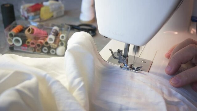 Elderly hands sew fabric behind the machine. A needle and thread stitches fabric close-up.