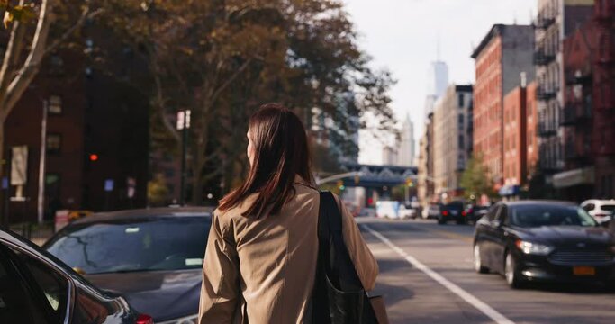 Rear view of attractive brunette female walking around urban autumnal streets of NYC lit by sunlight