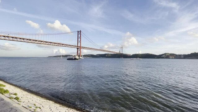 Lisbon 25th April red bridge, view from the waterfront, with Cristo Rei in background. Blue sky with clouds in winter