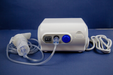 The electric nebulizer is white in color with a plastic tube and a device for inhaling medicines on a blue background. Medicine pulmonology technology.